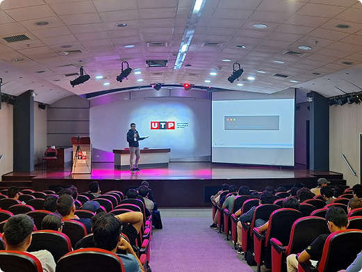 Ponente dando una charla en un auditorio universitario con una presentación proyectada en pantalla. El auditorio está lleno de asistentes, y en el fondo se ve el logo de la Universidad Tecnológica del Perú.